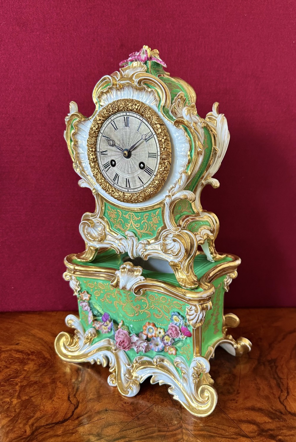 An early 19th-century French Rococo Revival porcelain mantel clock featuring green glaze, gilt scrollwork, and hand-moulded floral details.