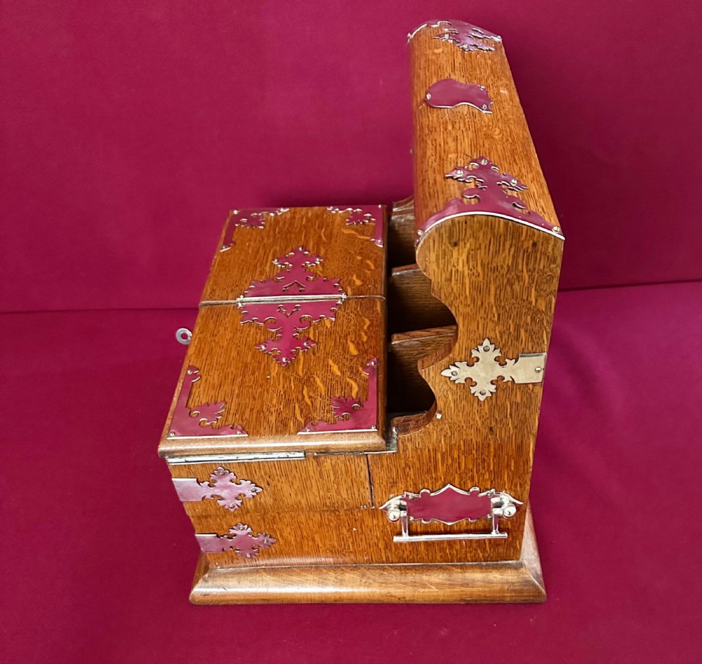 An opened Edwardian oak tantalus compendium box featuring three cut-glass decanters, a mirrored back, and hinged cantilever side compartments with silver-plated fittings. View IX