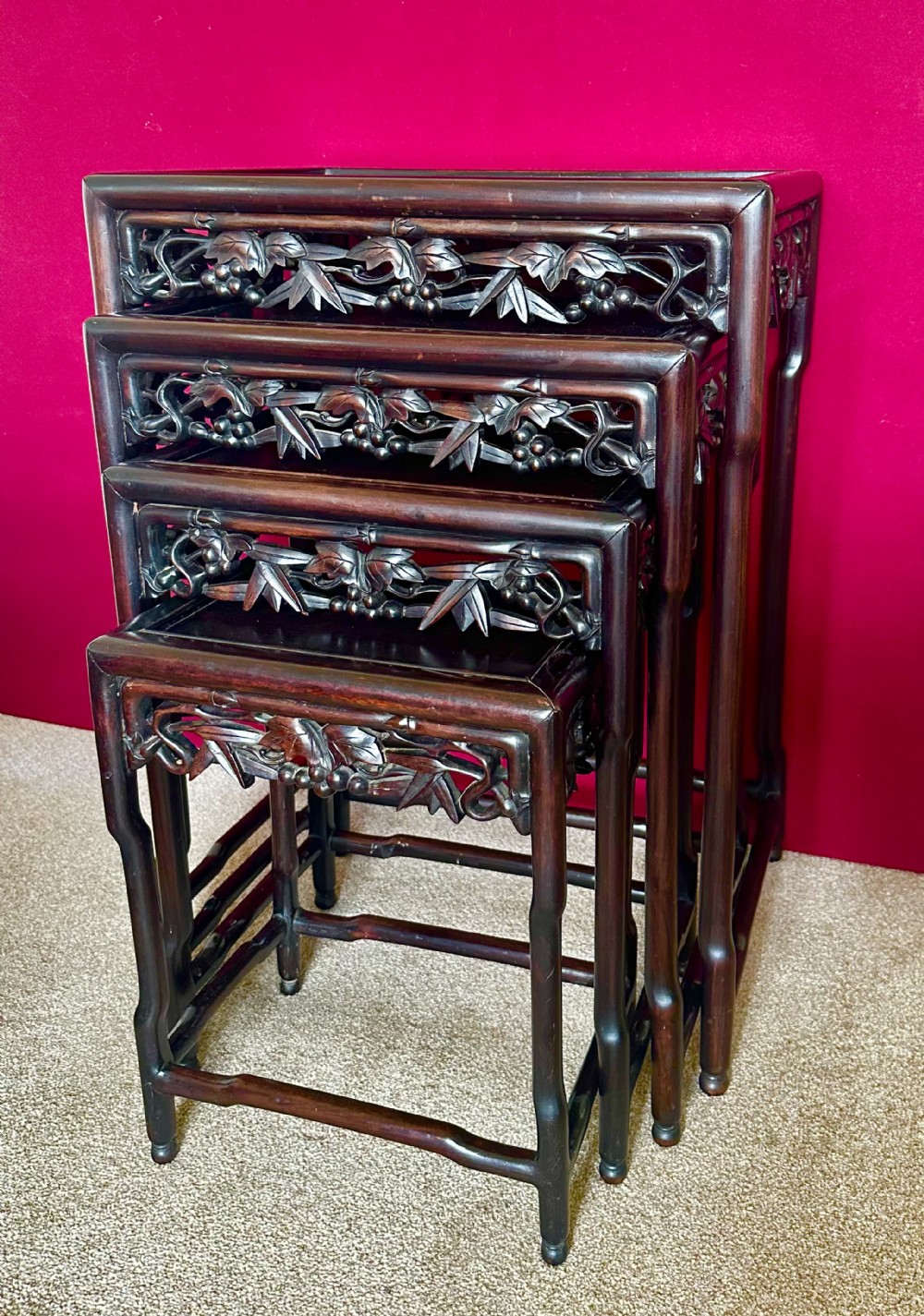 A set of four dark hardwood Chinese nesting tables featuring openwork carved bamboo aprons and faux-bamboo legs.