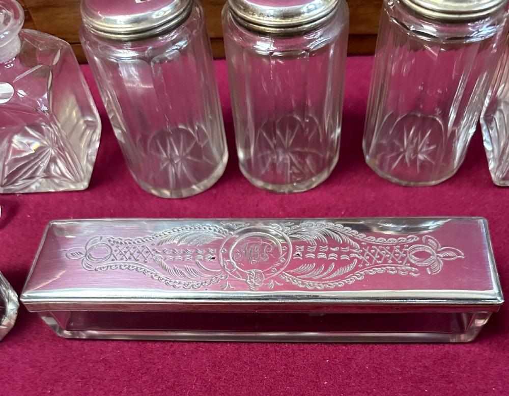 An open Victorian walnut travelling dressing case featuring an interior lid mirror, purple velvet compartments, glass jars with silver caps, and an opened lower drawer. View III