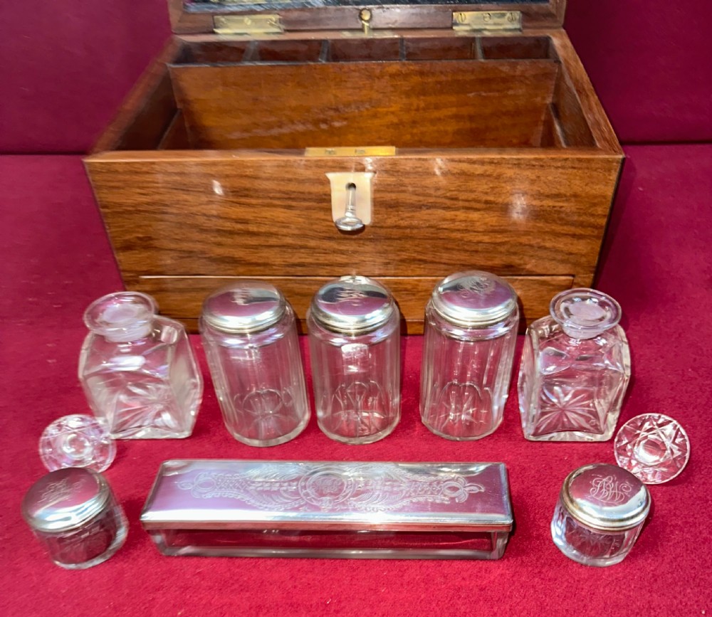 An open Victorian walnut travelling dressing case featuring an interior lid mirror, purple velvet compartments, glass jars with silver caps, and an opened lower drawer. View VIII