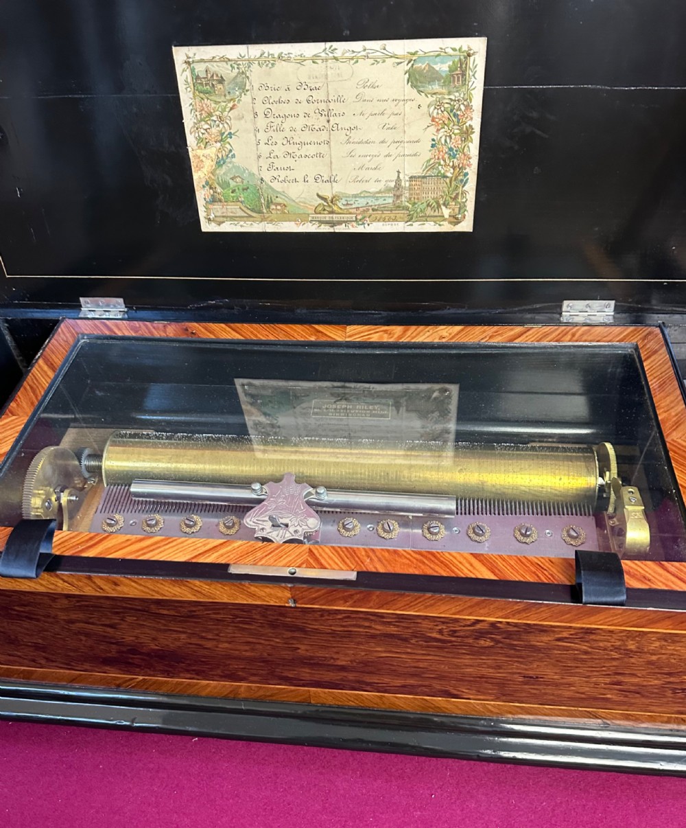 A rectangular Victorian wooden music box featuring rich wood veneers, ebonised trim, and a central marquetry inlay depicting figures on the lid. View III