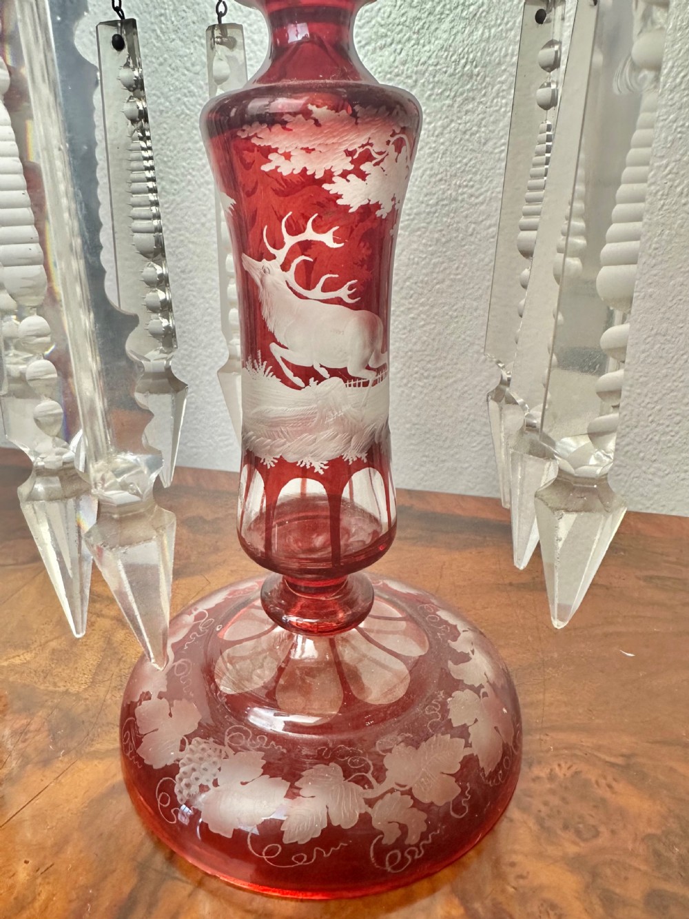 A pair of 19th-century Victorian ruby red flash glass lustres with acid-etched stag scenes, scalloped rims, and suspended clear crystal prism drops. View V