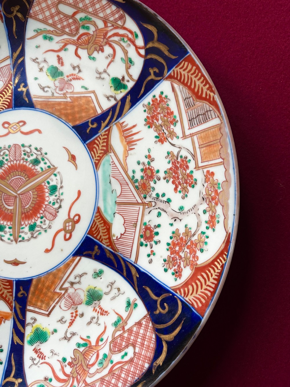 A circular Japanese Imari porcelain charger featuring cobalt blue and iron-red panelled decorations with floral motifs and phoenix figures. View V