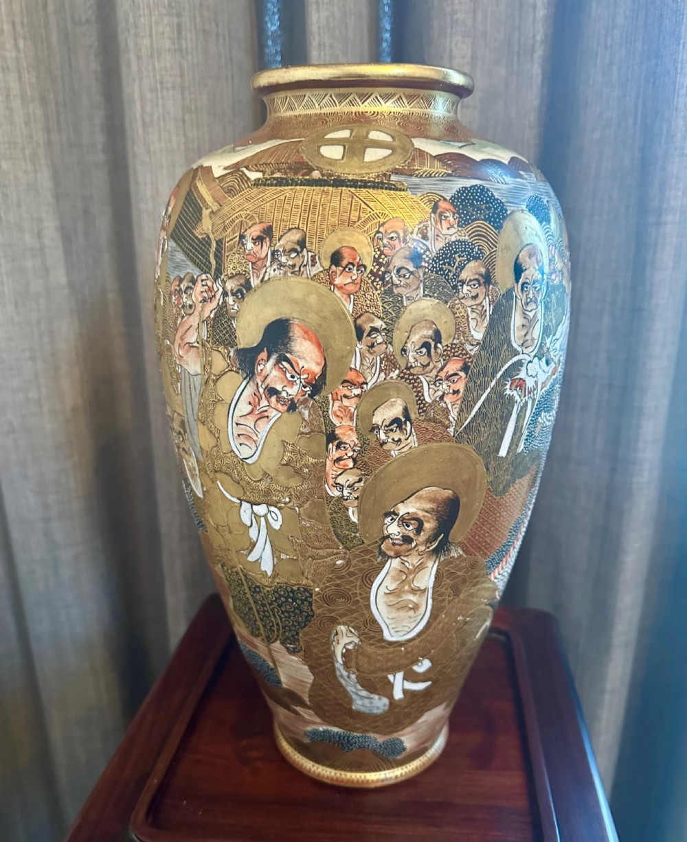 A large Japanese Satsuma earthenware vase featuring detailed hand-painted figures with halos, highlighted with heavy gold leaf accents.