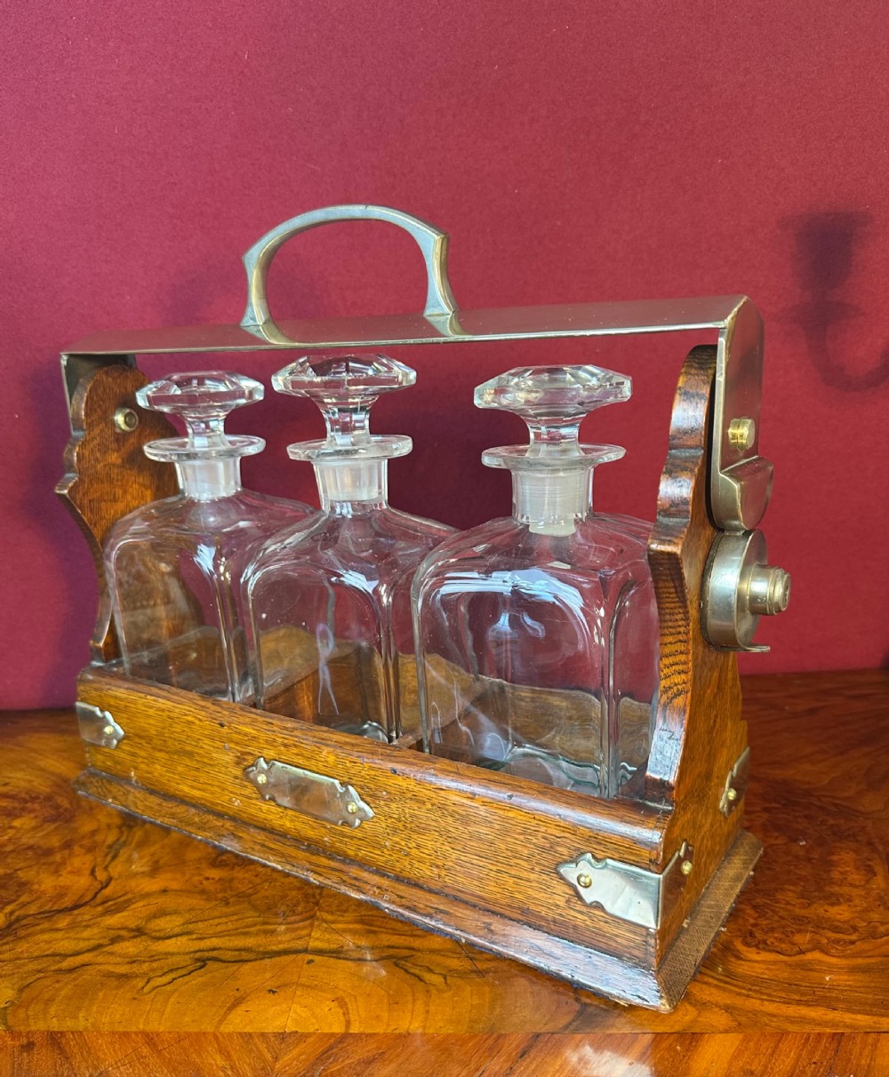 An Edwardian oak decanter tantalus featuring three square cut-glass decanters enclosed within a wooden frame with a metal handle and lock mechanism.