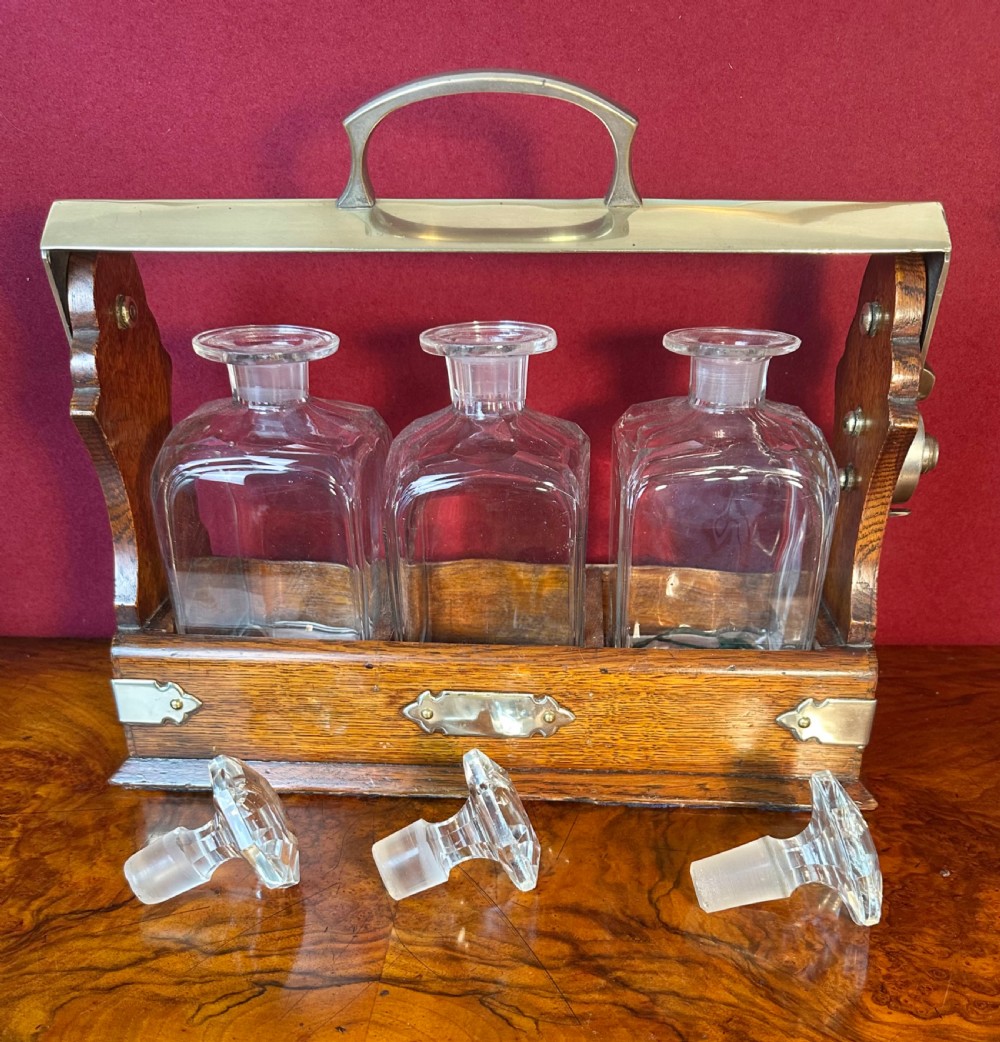 An Edwardian oak decanter tantalus featuring three square cut-glass decanters enclosed within a wooden frame with a metal handle and lock mechanism. View V