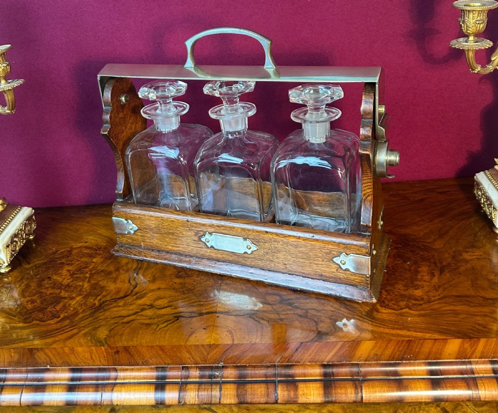 An Edwardian oak decanter tantalus featuring three square cut-glass decanters enclosed within a wooden frame with a metal handle and lock mechanism. View VI