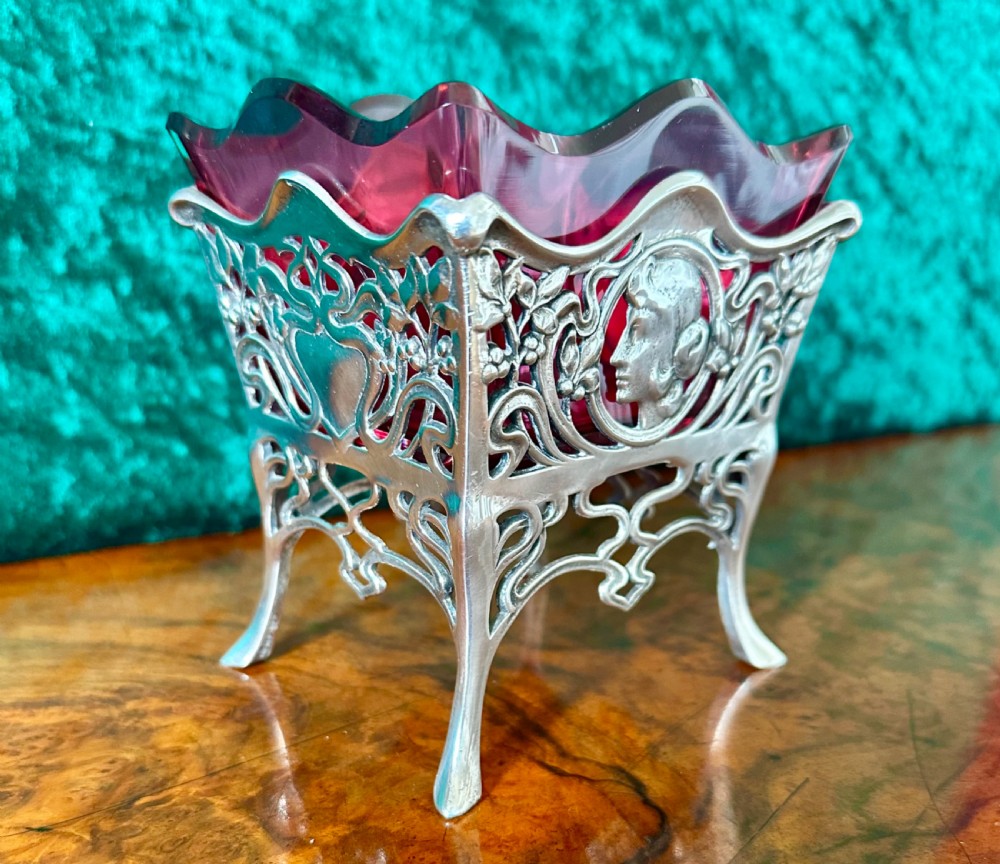 An Art Nouveau silver-plated pierced metal frame featuring a maiden profile with a ruby red glass liner.