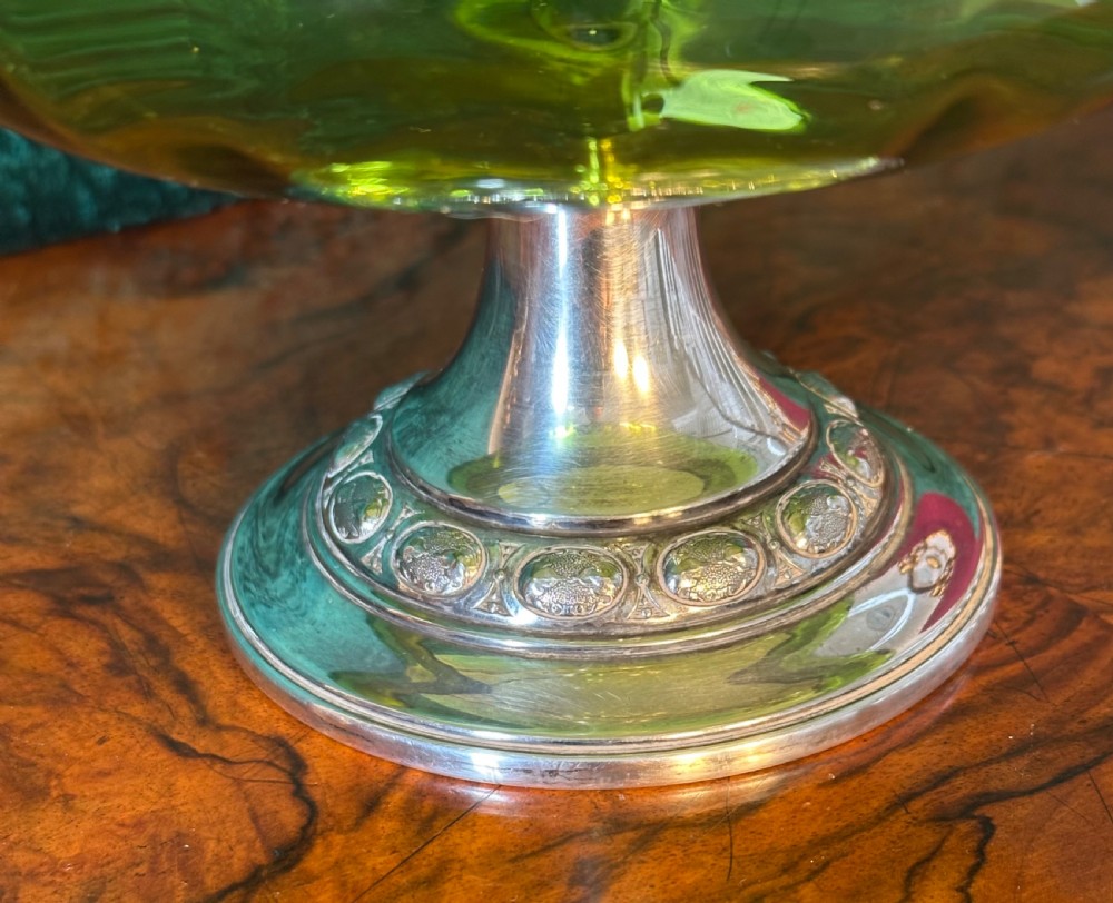 An Art Nouveau silver-plated pedestal basket featuring an ornate swing handle, pierced filigree decorative band, and a green glass liner. View V