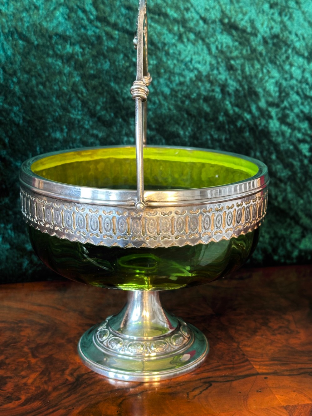An Art Nouveau silver-plated pedestal basket featuring an ornate swing handle, pierced filigree decorative band, and a green glass liner. View VI