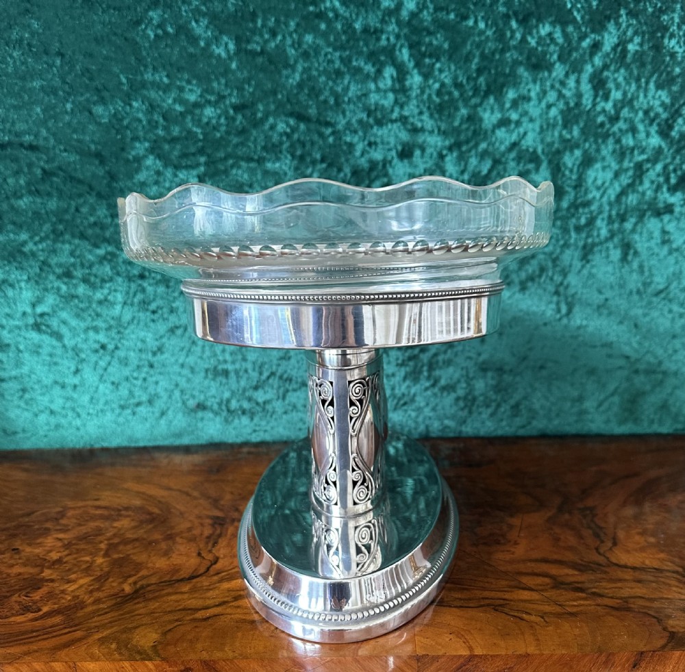 An oval silver-plated pedestal stand featuring openwork scroll panels and a clear glass dish with a scalloped rim. View III