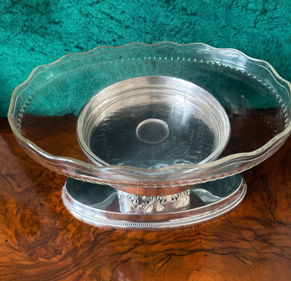 An oval silver-plated pedestal stand featuring openwork scroll panels and a clear glass dish with a scalloped rim. View VI