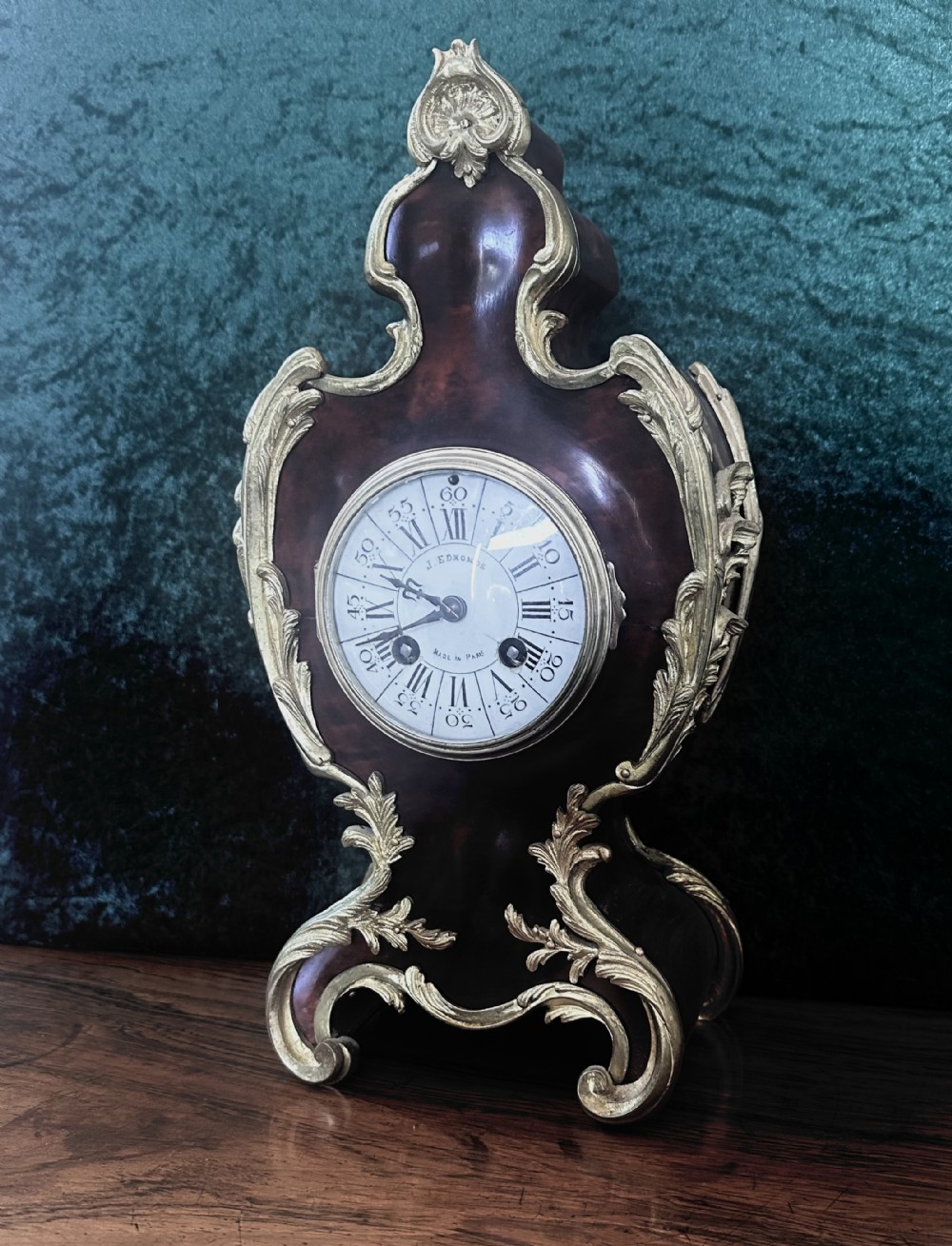 A 19th-century Victorian mantel clock in the Louis XV style featuring a dark veneered balloon case with gilded metal foliage mounts and a white enamel dial.