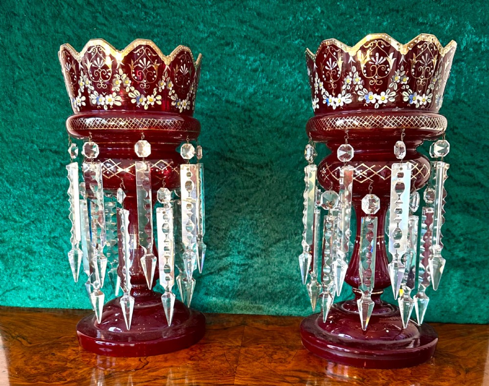 A pair of Victorian ruby red glass lustres featuring hand-painted enamel floral motifs, scalloped rims, and suspended clear cut-glass prism drops.