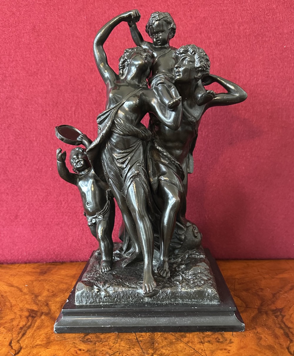 A dark patinated bronze figural sculpture depicting classical figures and putti dancing on a rectangular bronze base.