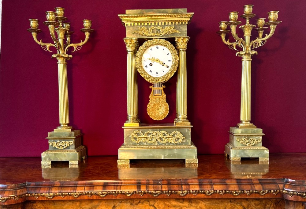 A 19th-century French clock garniture featuring a central portico-style green onyx mantel clock with gilt-bronze mounts flanked by two matching five-light candelabra.