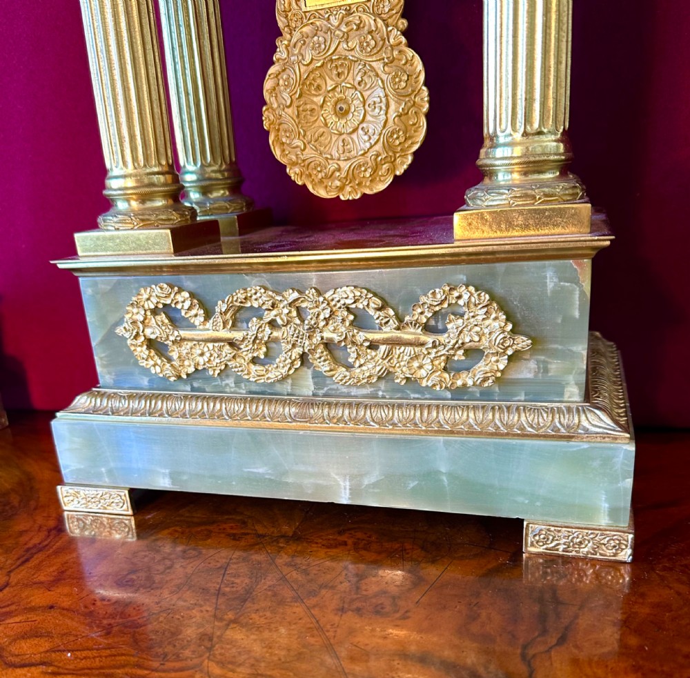 A 19th-century French clock garniture featuring a central portico-style green onyx mantel clock with gilt-bronze mounts flanked by two matching five-light candelabra. View V