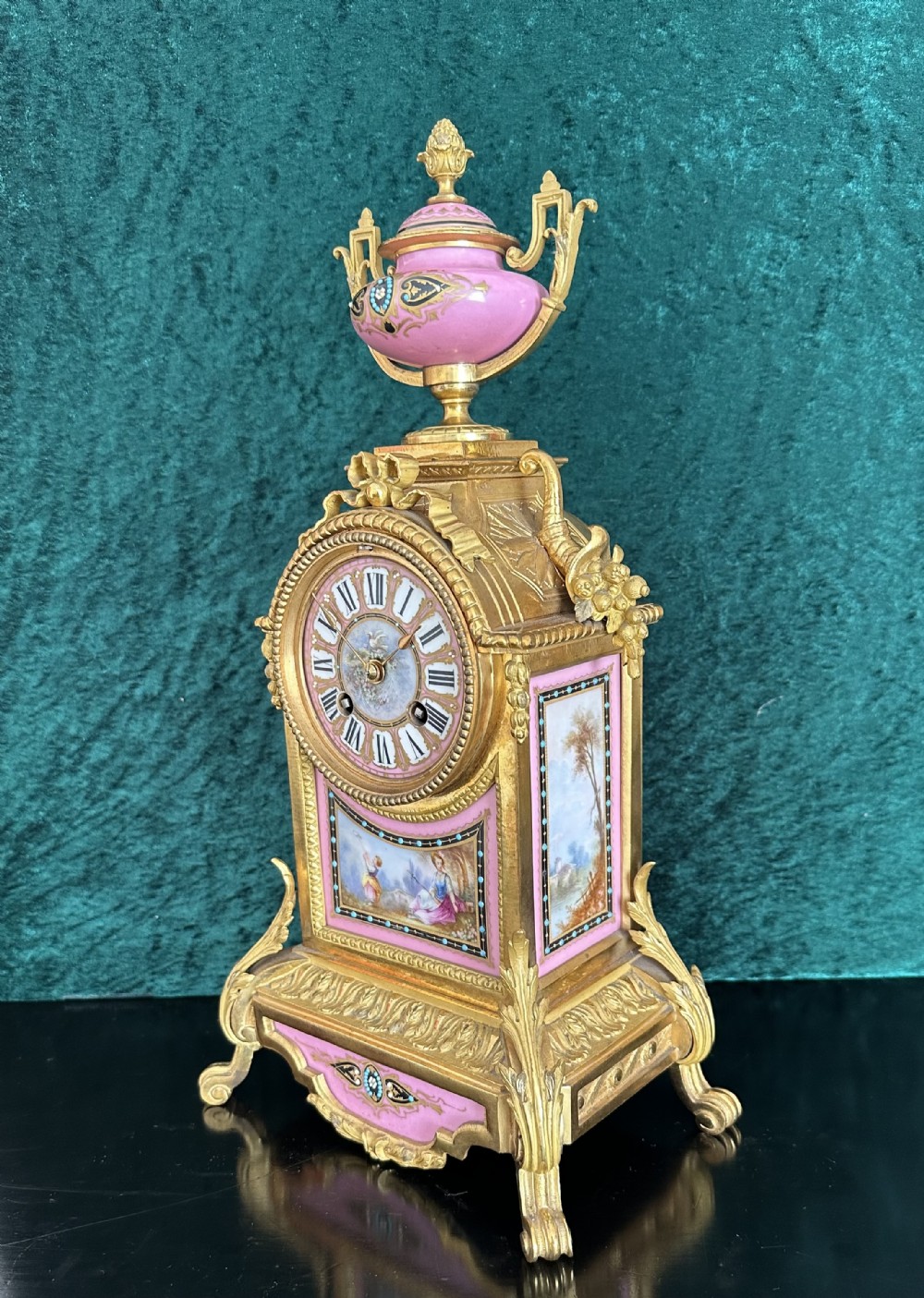 A late 19th-century French gilt bronze mantel clock featuring hand-painted pink porcelain panels, an urn finial, and an enamel dial with Roman numerals.