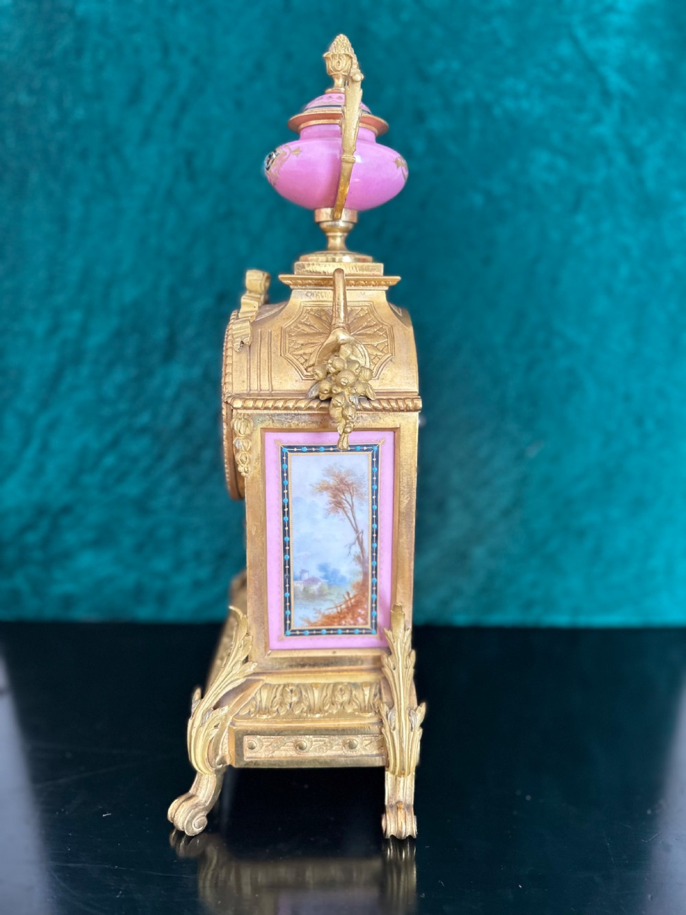 A late 19th-century French gilt bronze mantel clock featuring hand-painted pink porcelain panels, an urn finial, and an enamel dial with Roman numerals. View VI