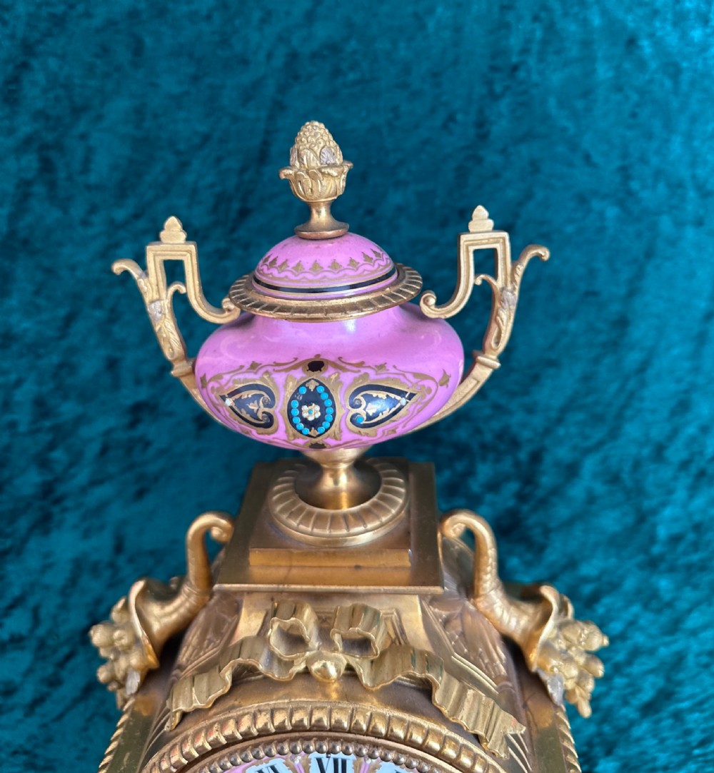 A late 19th-century French gilt bronze mantel clock featuring hand-painted pink porcelain panels, an urn finial, and an enamel dial with Roman numerals. View X
