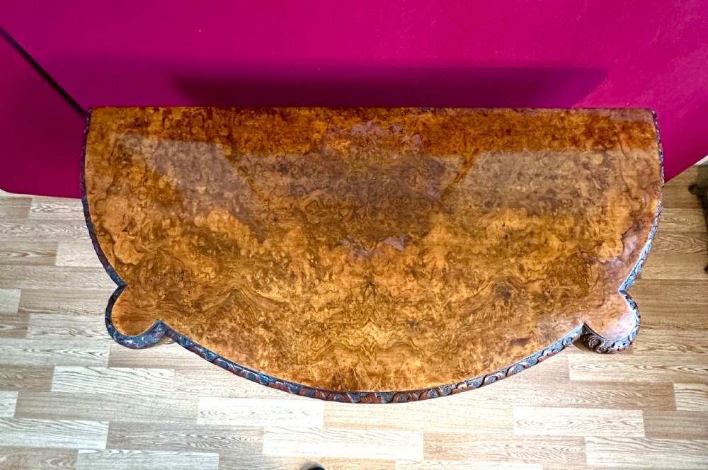 A Victorian burr walnut fold-over card table featuring a carved frieze, a central carved pedestal stem, and four cabriole legs on ceramic castors. View III
