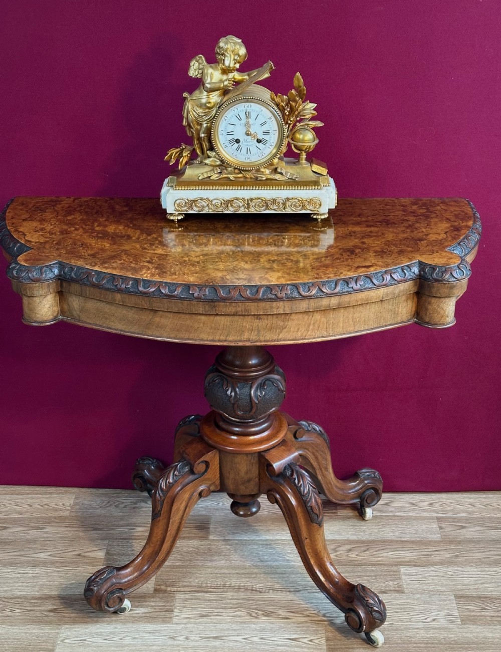 A Victorian burr walnut fold-over card table featuring a carved frieze, a central carved pedestal stem, and four cabriole legs on ceramic castors. View VI