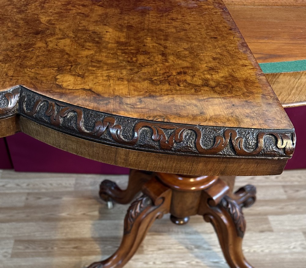 A Victorian burr walnut fold-over card table featuring a carved frieze, a central carved pedestal stem, and four cabriole legs on ceramic castors. View IX