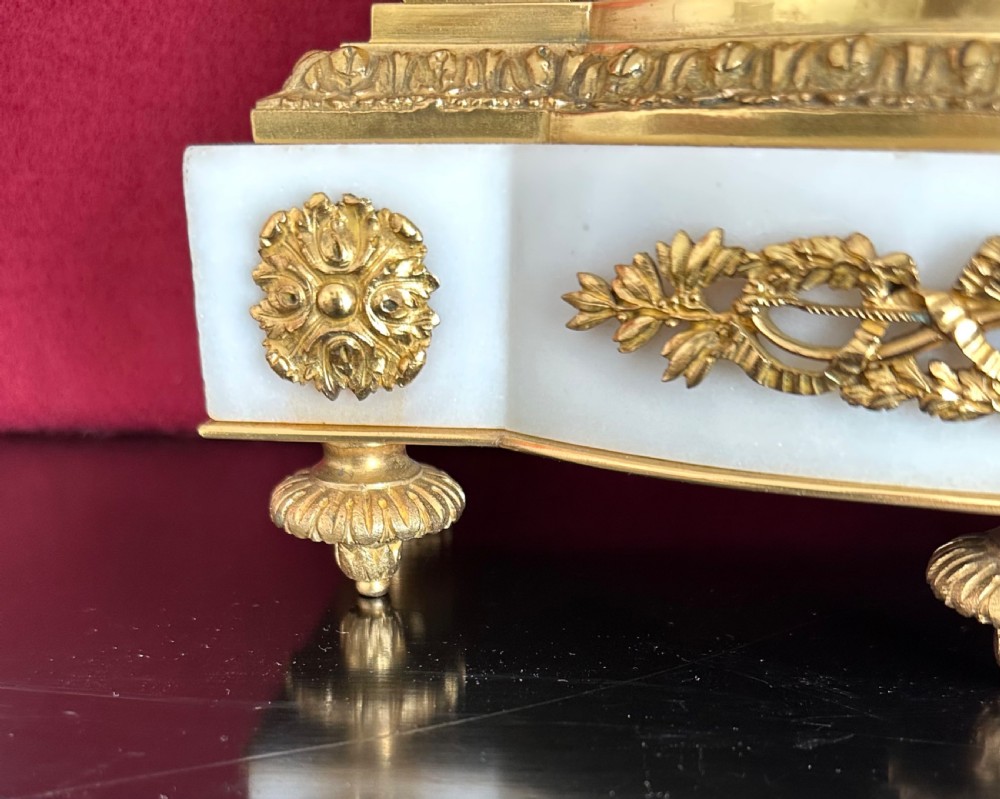 A late nineteenth-century French Louis XVI revival mantel clock made of gilt ormolu and white marble, featuring putti figures flanking a white enamel dial. View XVII
