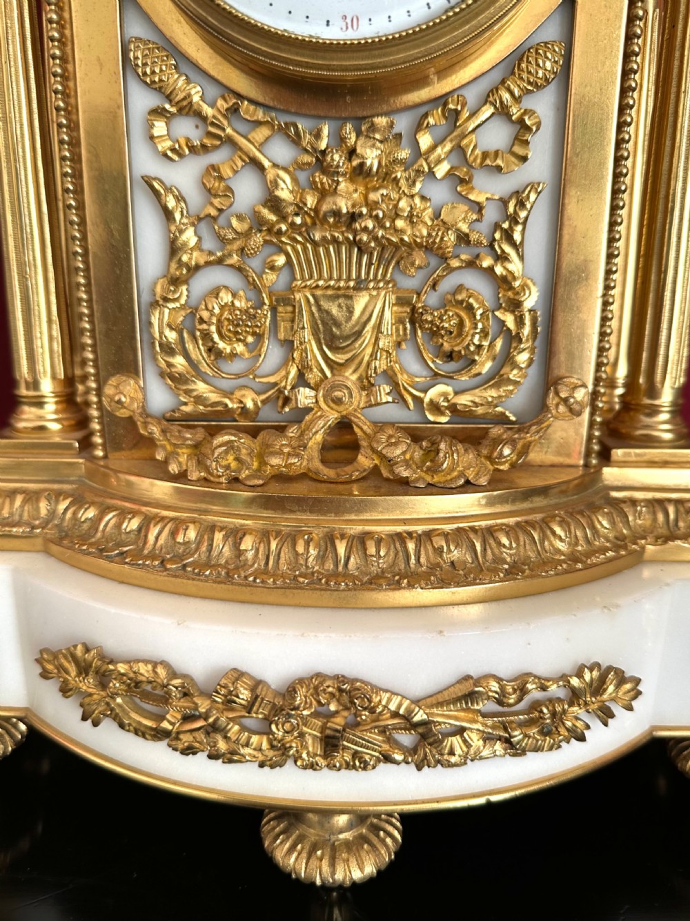 A late nineteenth-century French Louis XVI revival mantel clock made of gilt ormolu and white marble, featuring putti figures flanking a white enamel dial. View XVIII