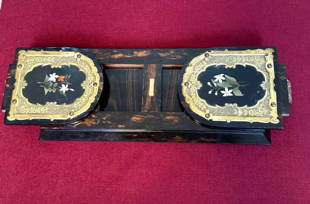 An expanding Victorian desk book slide crafted from dark coromandel wood, featuring hinged arch-shaped ends set with pietra dura floral stone inlays surrounded by engraved brass mounts.