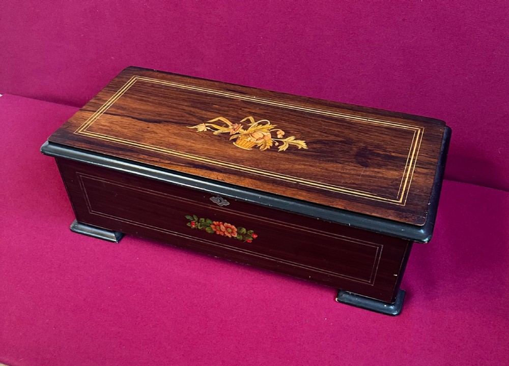 A rectangular Victorian dark rosewood music box featuring floral marquetry inlay on the lid and ebonised corner feet.