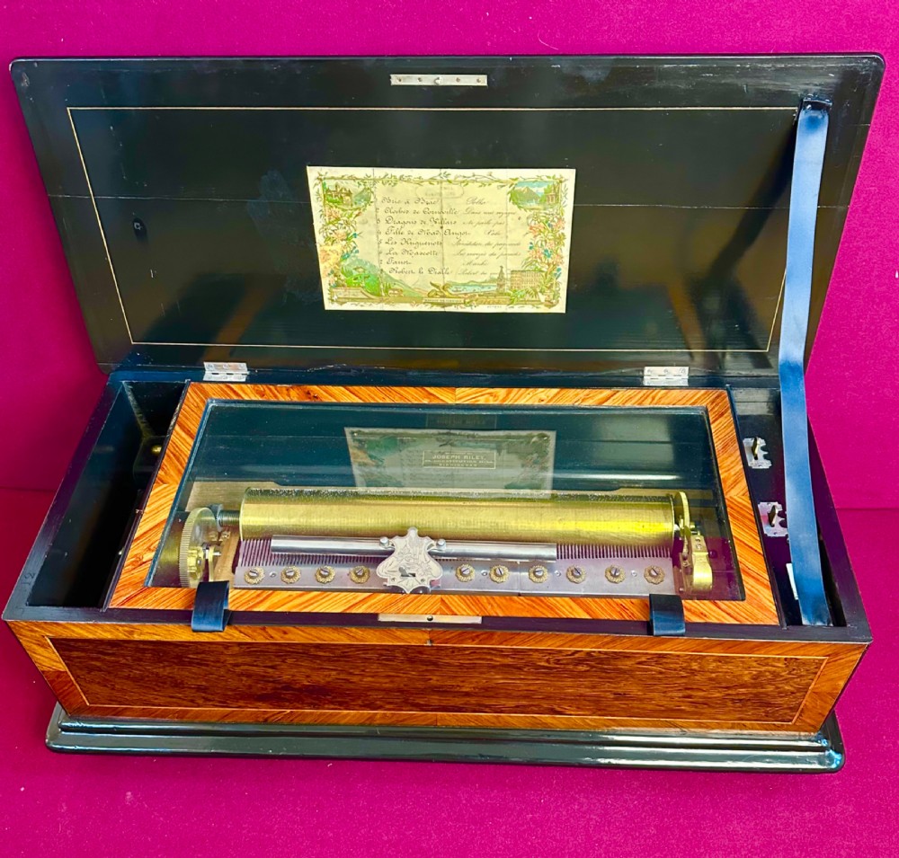A Victorian wooden music box with an open lid displaying a printed tune sheet, brass cylinder mechanism, steel comb, and glass dust cover.