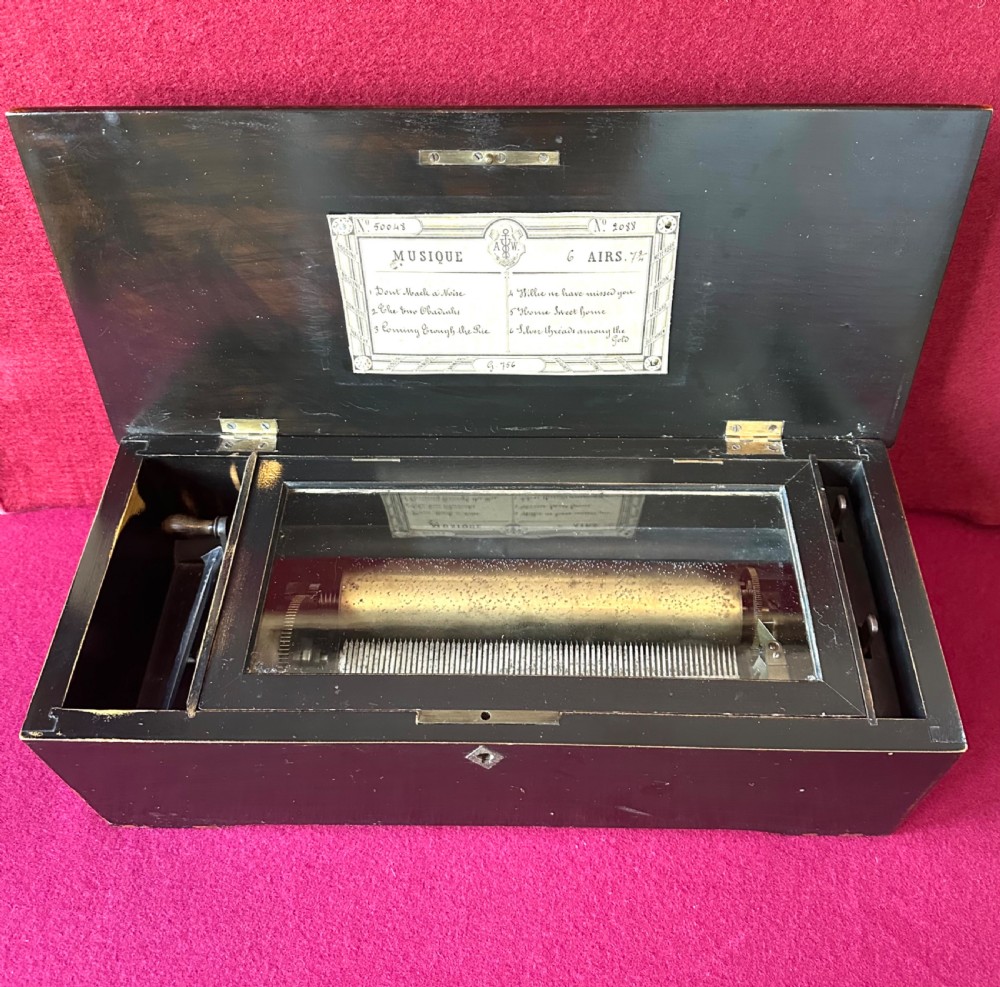 A Victorian ebonised wood music box shown with its hinged lid open, revealing a printed tune card and an internal glass cover over a brass cylinder and steel comb mechanism.