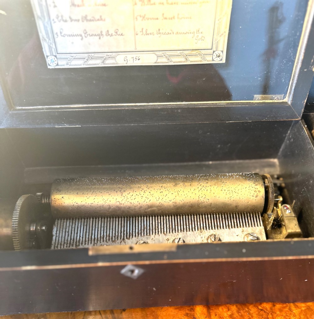 A Victorian ebonised wood music box shown with its hinged lid open, revealing a printed tune card and an internal glass cover over a brass cylinder and steel comb mechanism. View III