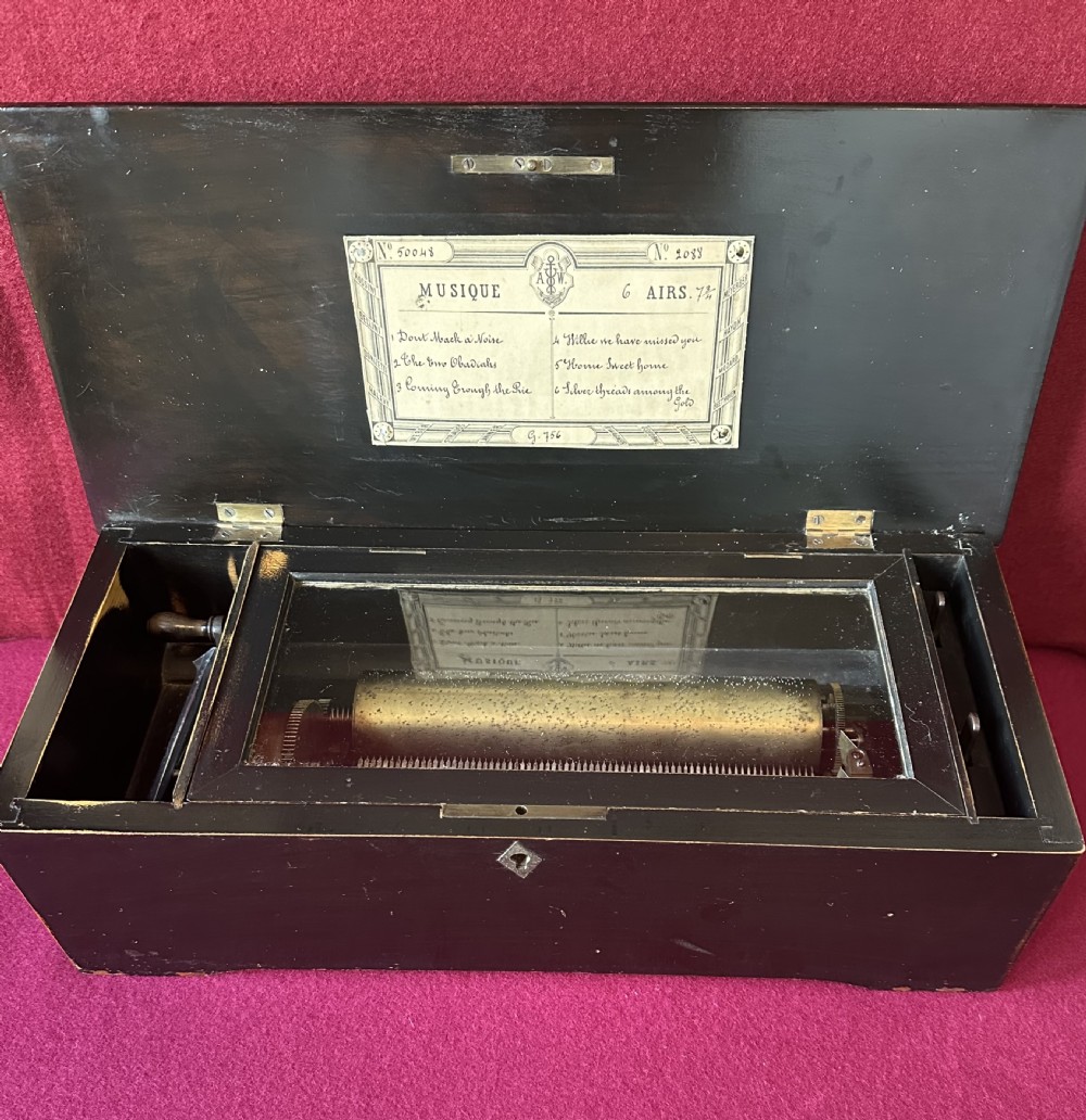 A Victorian ebonised wood music box shown with its hinged lid open, revealing a printed tune card and an internal glass cover over a brass cylinder and steel comb mechanism. View VI