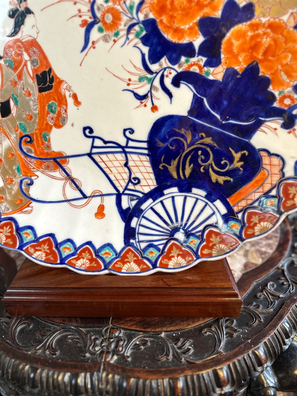 A circular Japanese Imari porcelain charger decorated with hand-painted human figures, floral arrangements, and a scalloped border in cobalt blue, rust red, and gold. View III