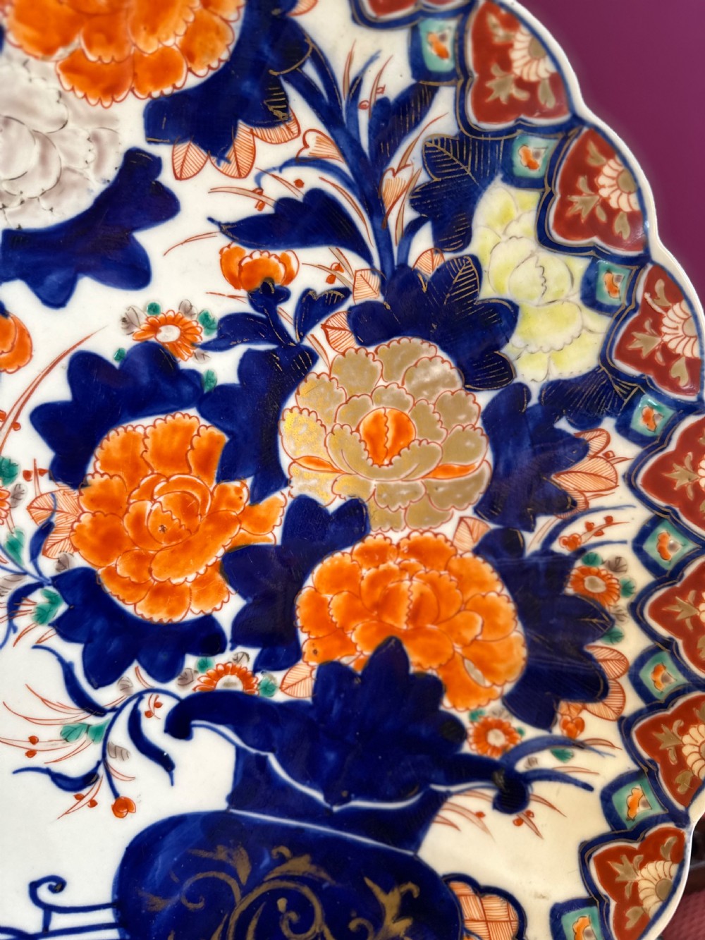 A circular Japanese Imari porcelain charger decorated with hand-painted human figures, floral arrangements, and a scalloped border in cobalt blue, rust red, and gold. View V