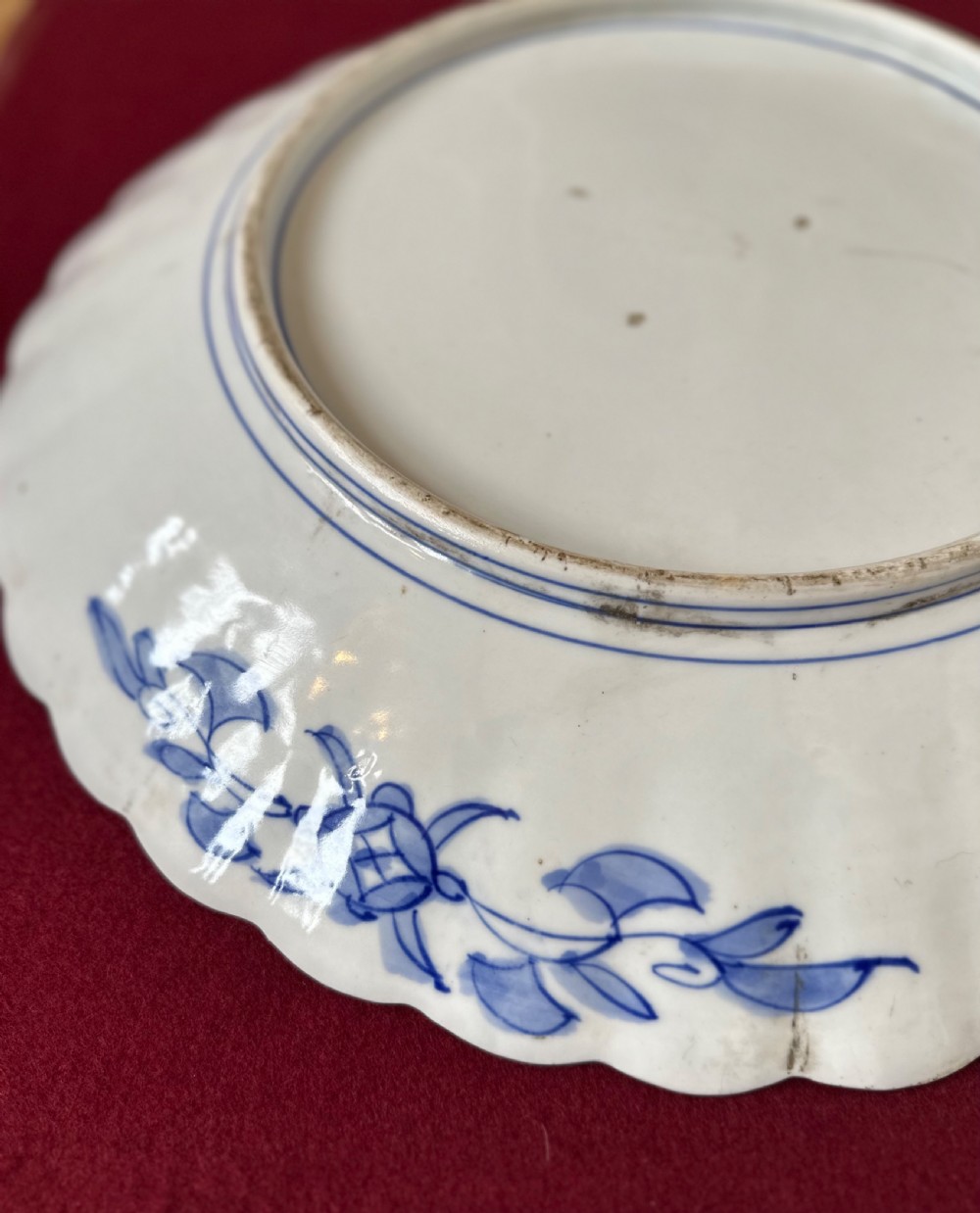 A circular Japanese Imari porcelain charger decorated with hand-painted human figures, floral arrangements, and a scalloped border in cobalt blue, rust red, and gold. View VI