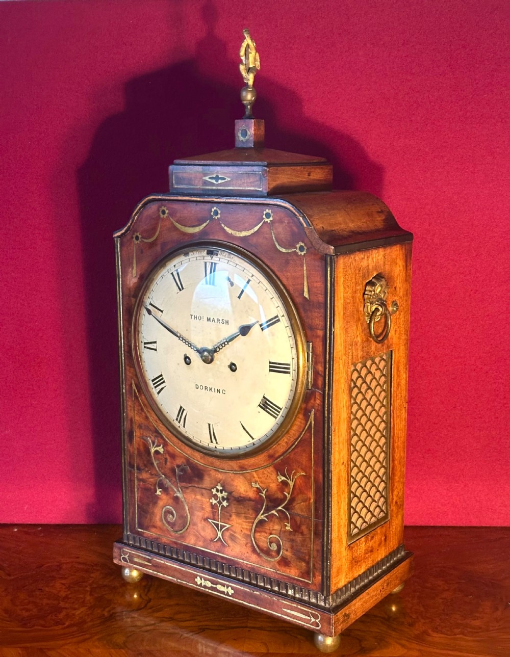 A Georgian mahogany bracket clock featuring brass inlay, lion mask handles, a top brass finial, and a circular dial signed Thos Marsh Dorking.