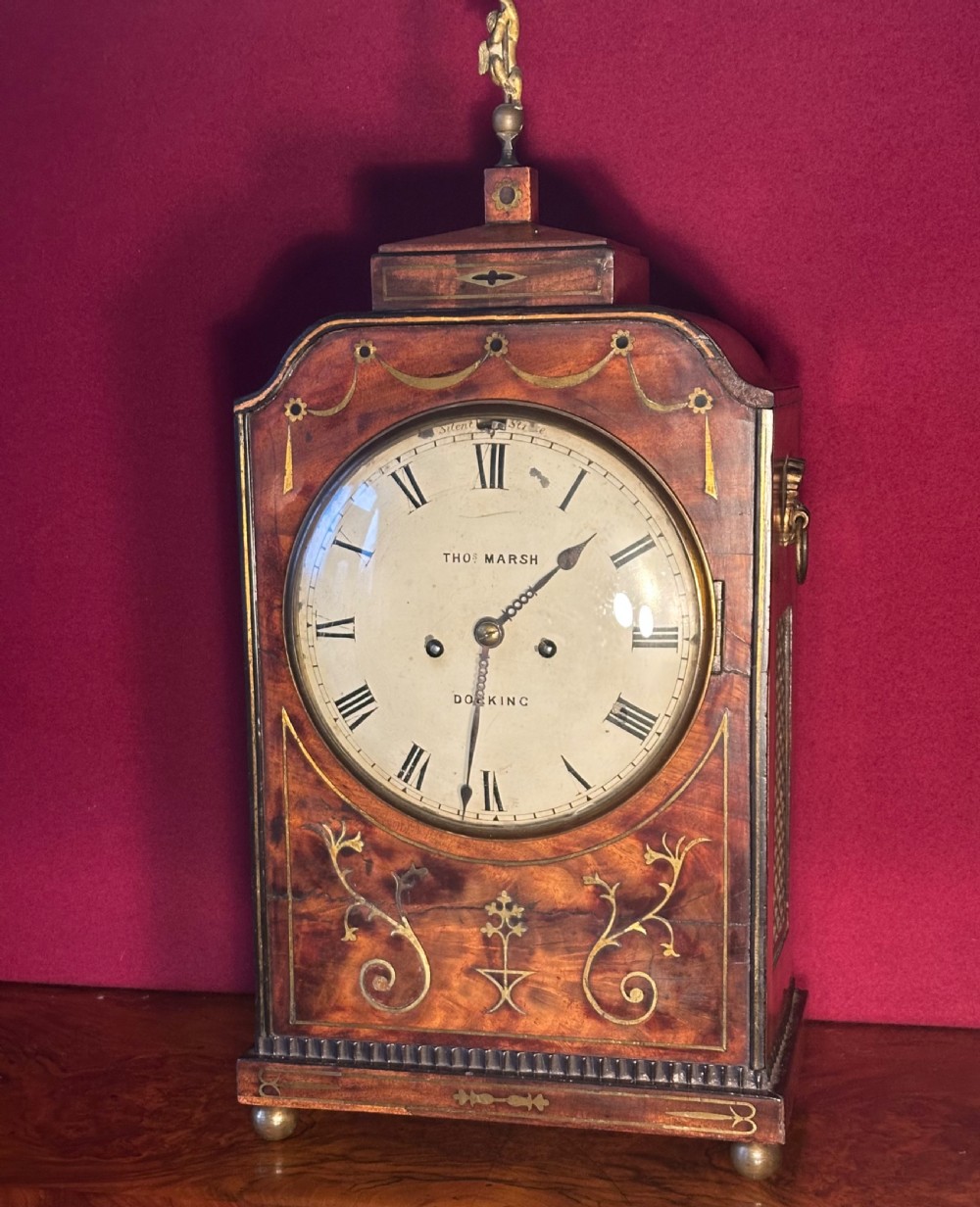 A Georgian mahogany bracket clock featuring brass inlay, lion mask handles, a top brass finial, and a circular dial signed Thos Marsh Dorking. View V