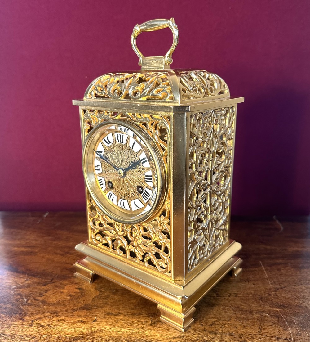 A late Victorian gilded brass mantel clock featuring intricate pierced fretwork side panels, a top carrying handle, and an engraved dial with white enamel Roman numeral markers.