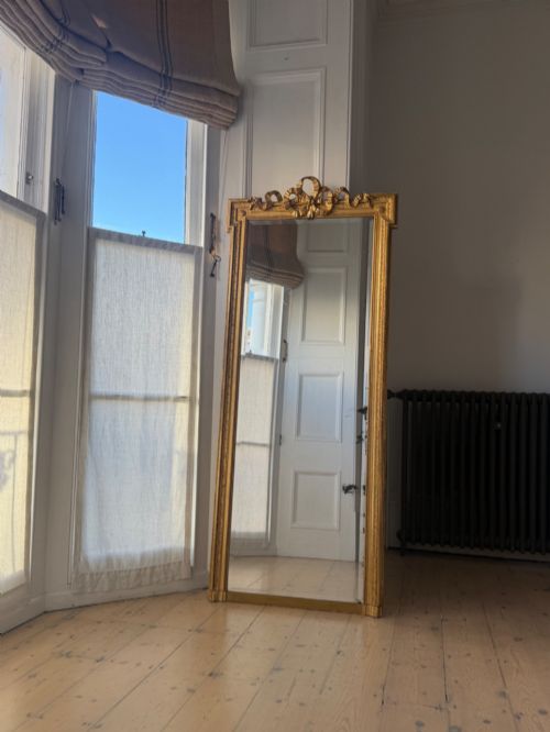fig 1. A tall rectangular gold giltwood full-length mirror featuring a carved bow ribbon cresting, beaded inner frame, and bevelled glass plate.