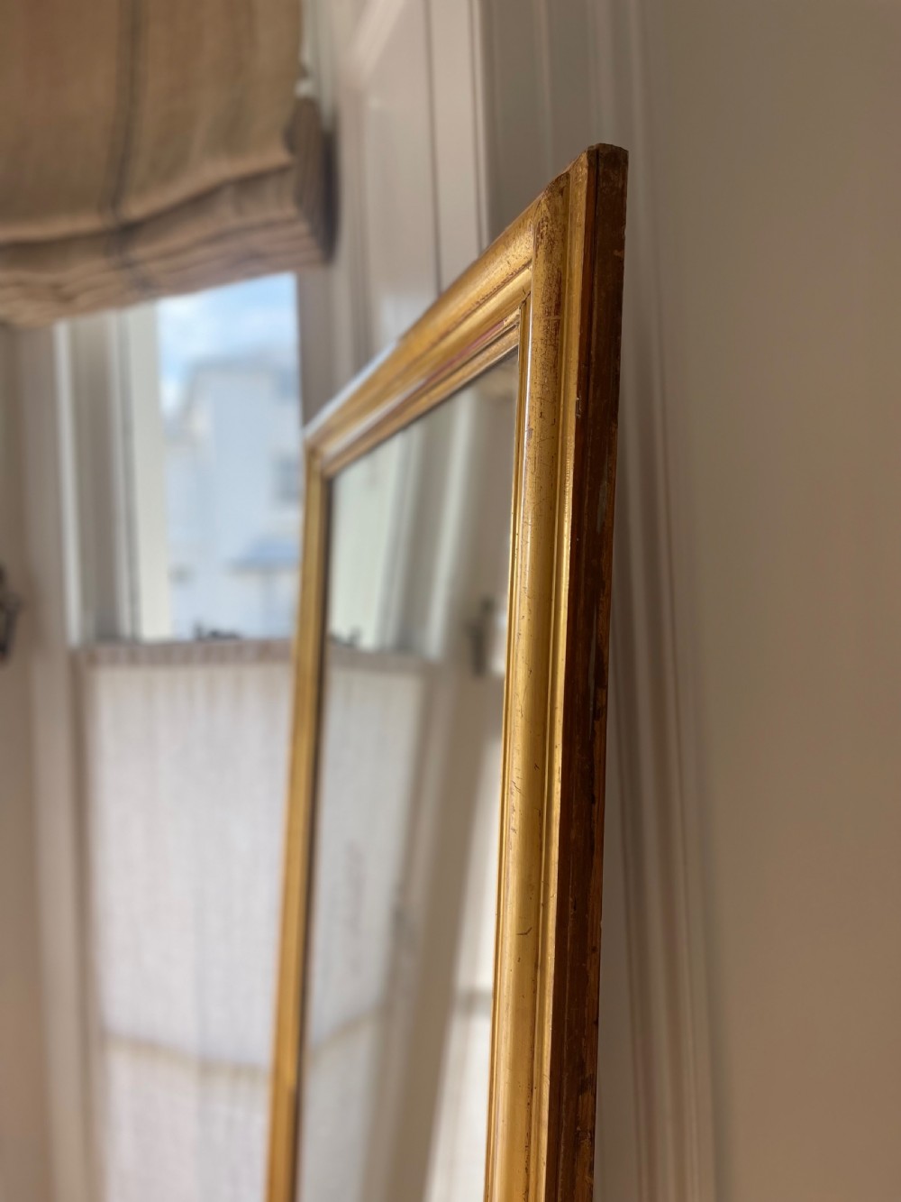 A tall antique French leaner mirror with an ornate gilded wooden frame resting on a wooden floor. View III