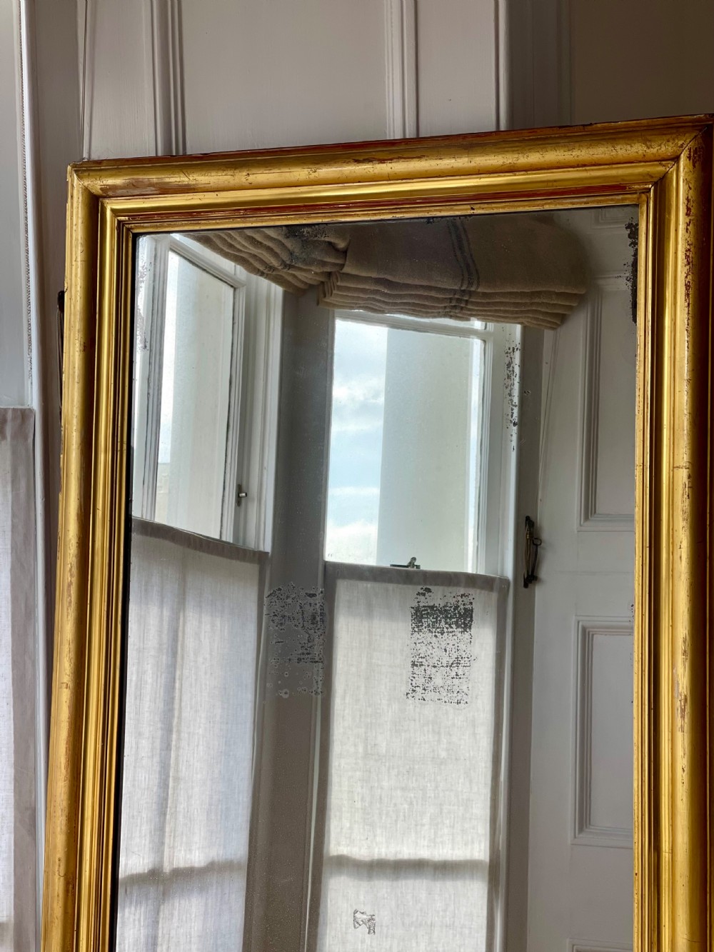 A tall antique French leaner mirror with an ornate gilded wooden frame resting on a wooden floor. View IV