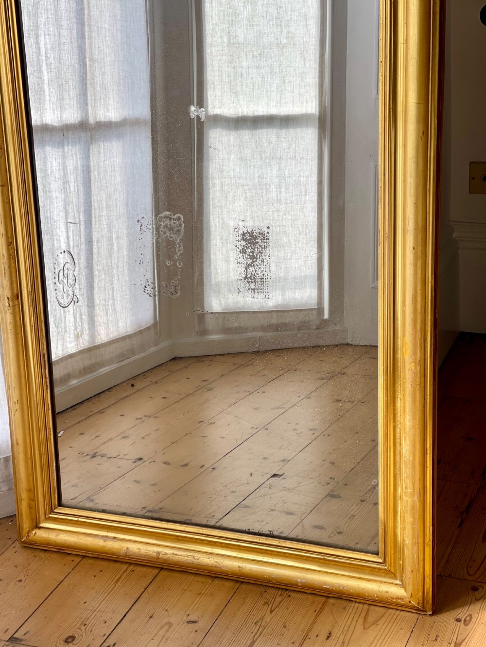 A tall antique French leaner mirror with an ornate gilded wooden frame resting on a wooden floor. View V