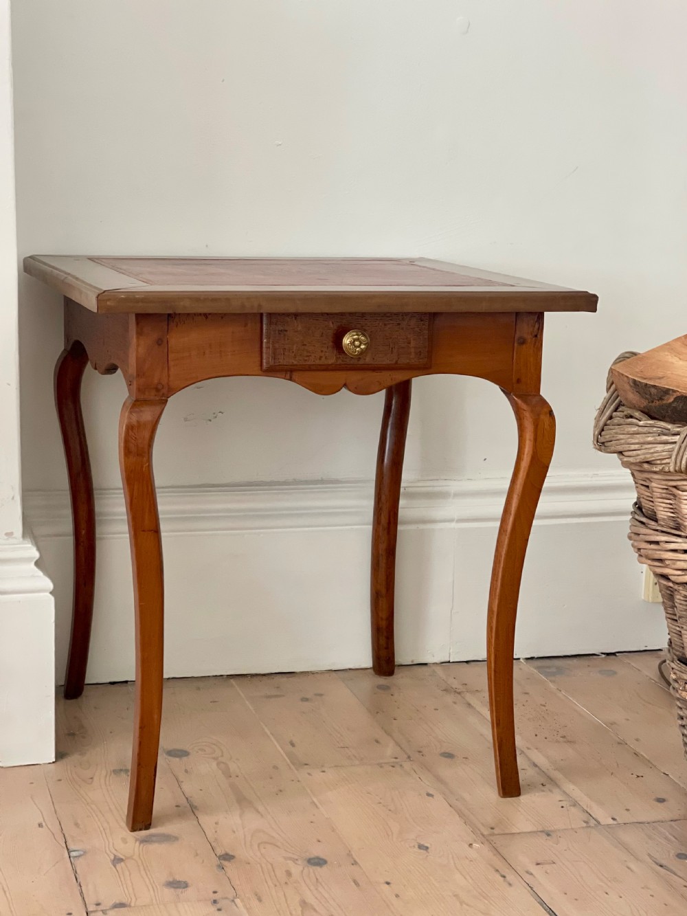 An antique French side table featuring a warm brown leather inset top, slender cabriole legs, and a single drawer with a brass knob.