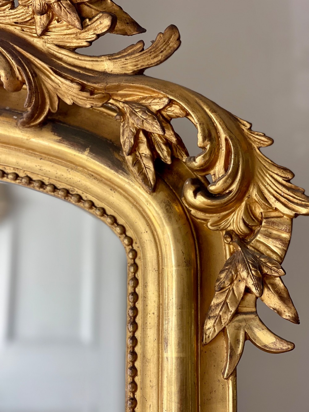A tall antique French giltwood overmantel mirror featuring an arched frame topped with an ornate carved crest. View II