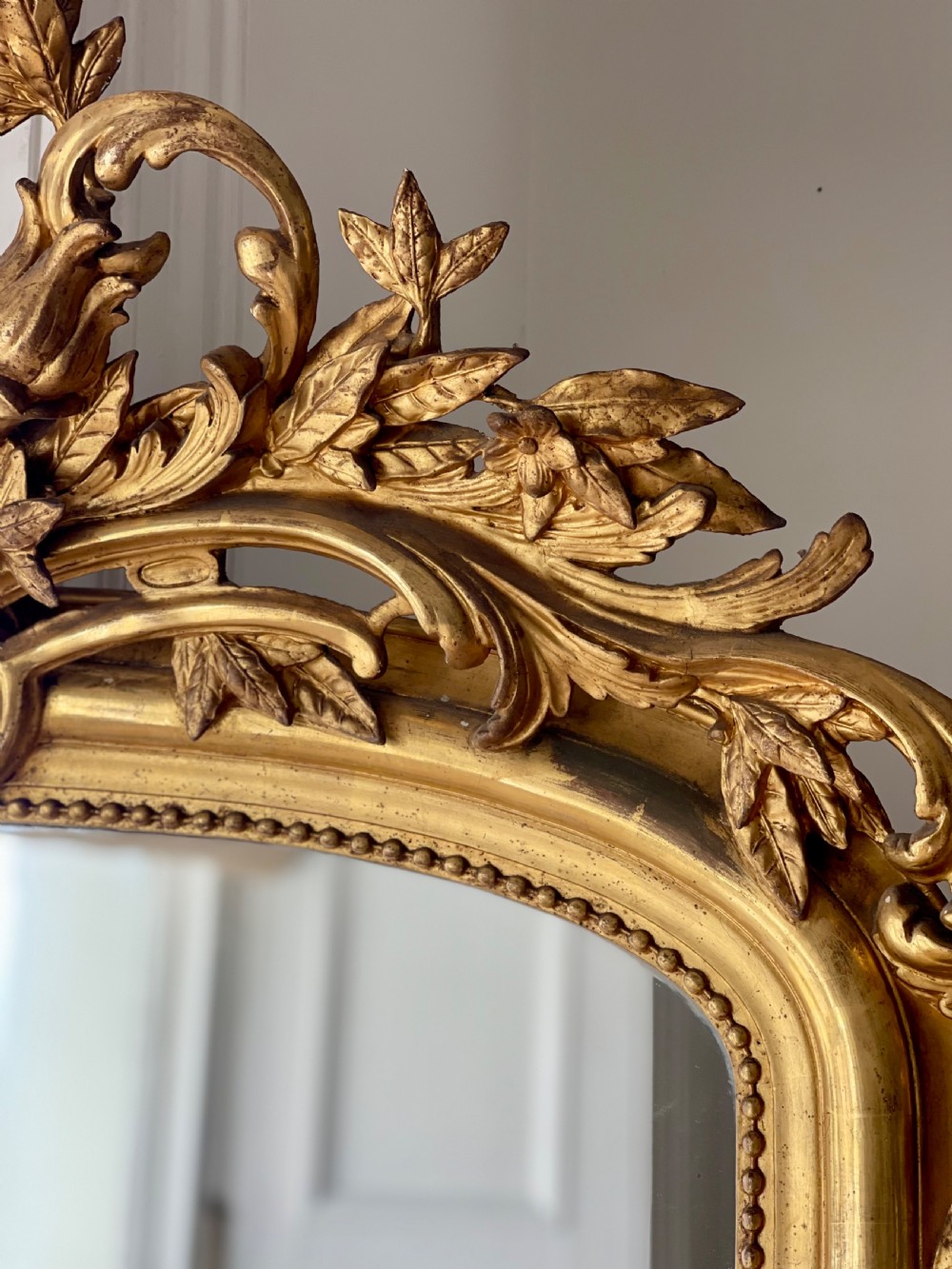 A tall antique French giltwood overmantel mirror featuring an arched frame topped with an ornate carved crest. View III