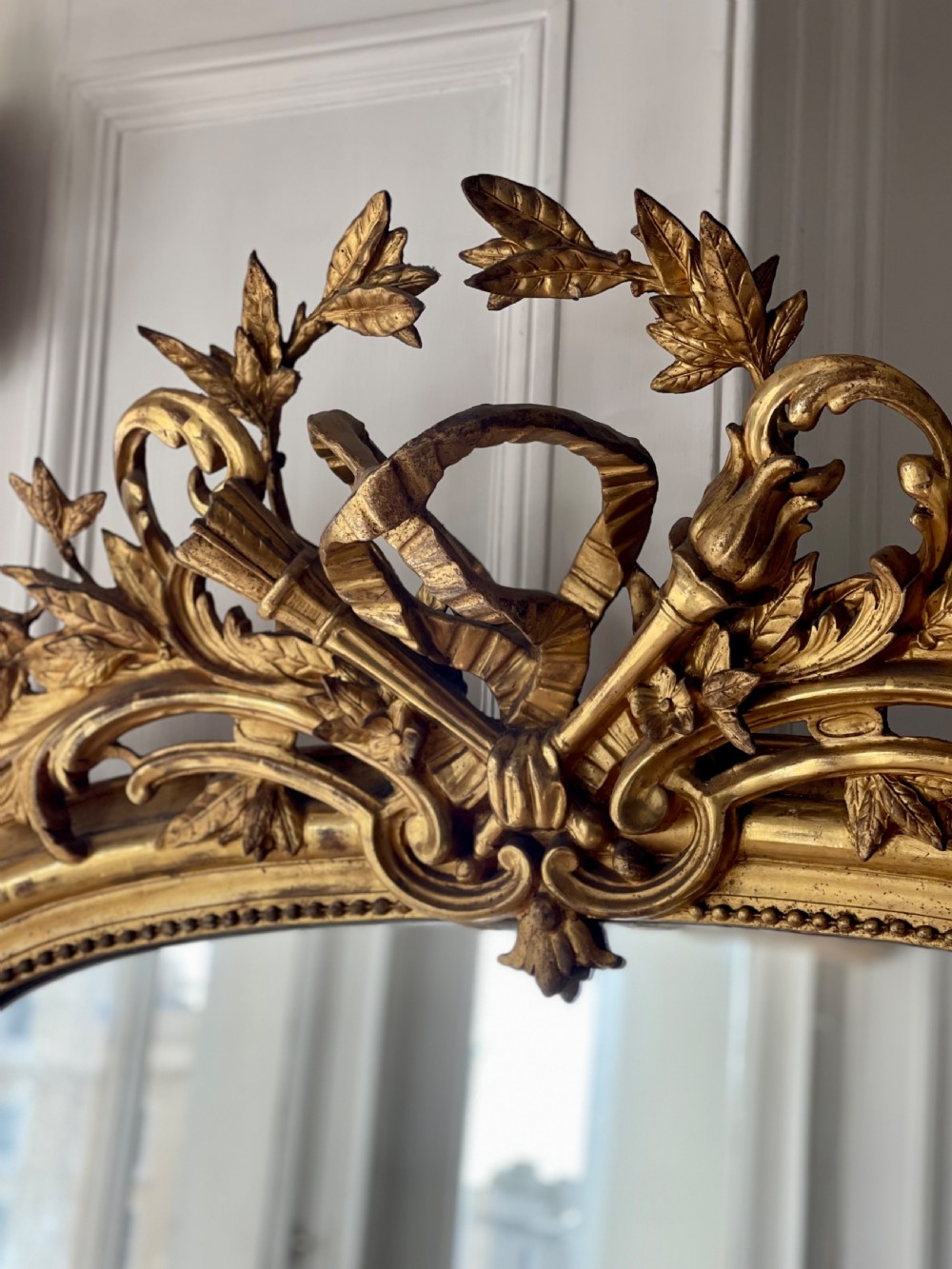 A tall antique French giltwood overmantel mirror featuring an arched frame topped with an ornate carved crest. View IV